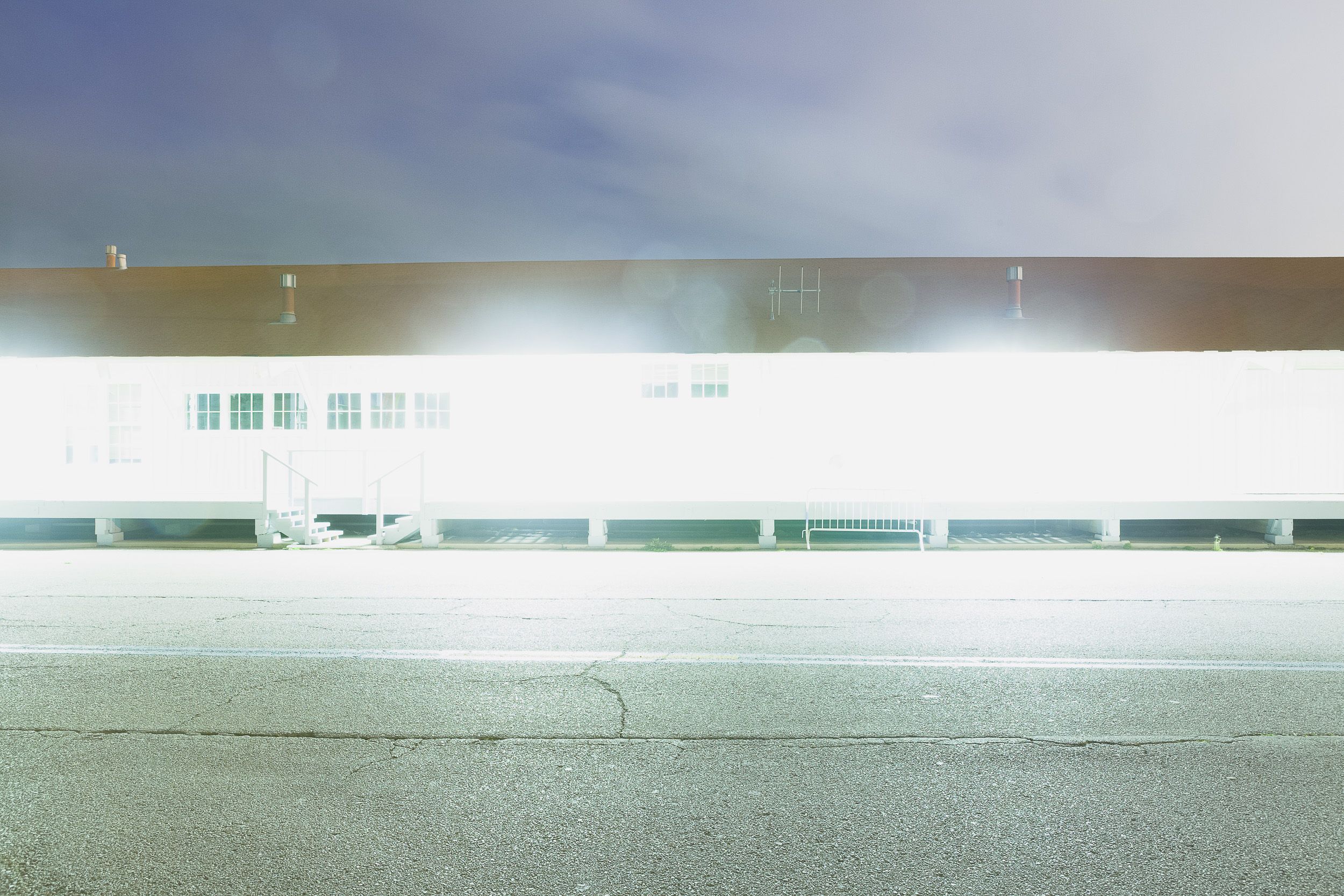 Long white industrial building exterior illuminated at night with bright lighting.