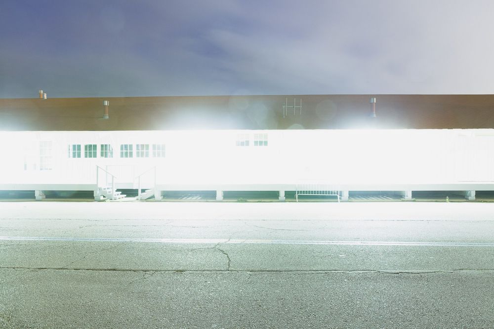 Long white industrial building exterior illuminated at night with bright lighting.