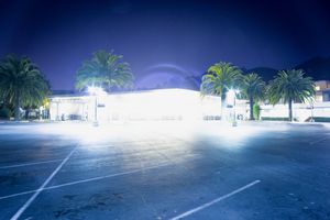 Illuminated parking lot and building exterior at night with palm trees.