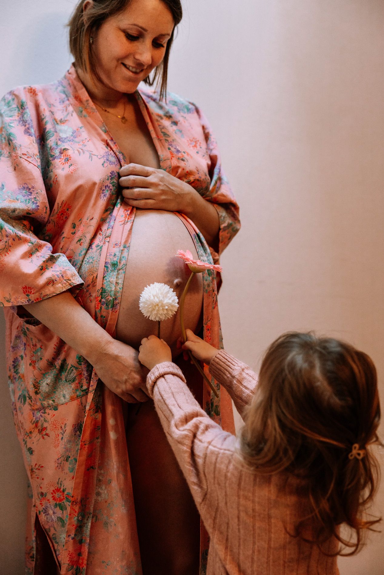 A touching maternity moment captured in floral pink robe as a child interacts with the pregnant belly.
