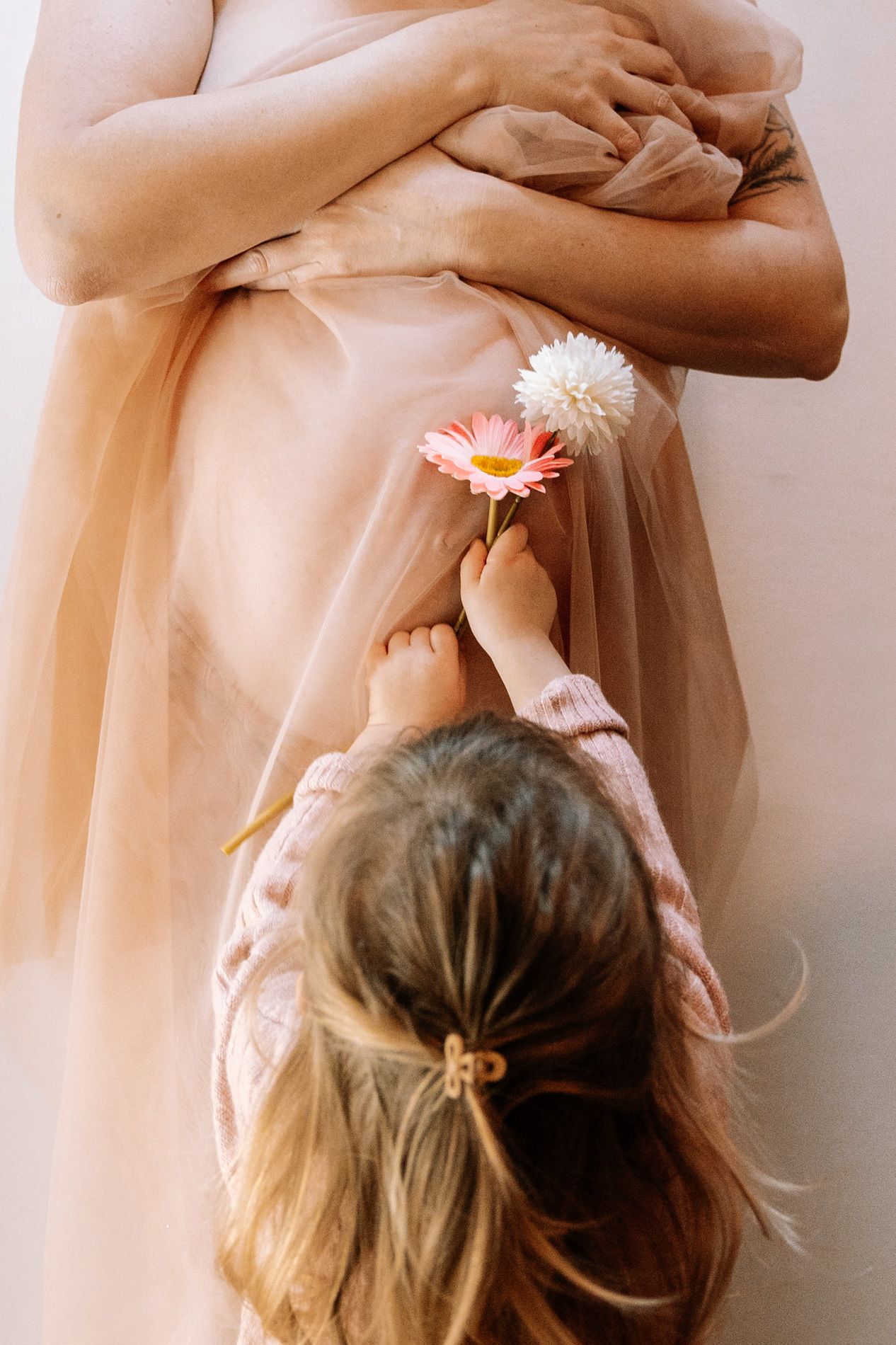 A series of delicate pink flowers being placed in long dark hair against a light background.