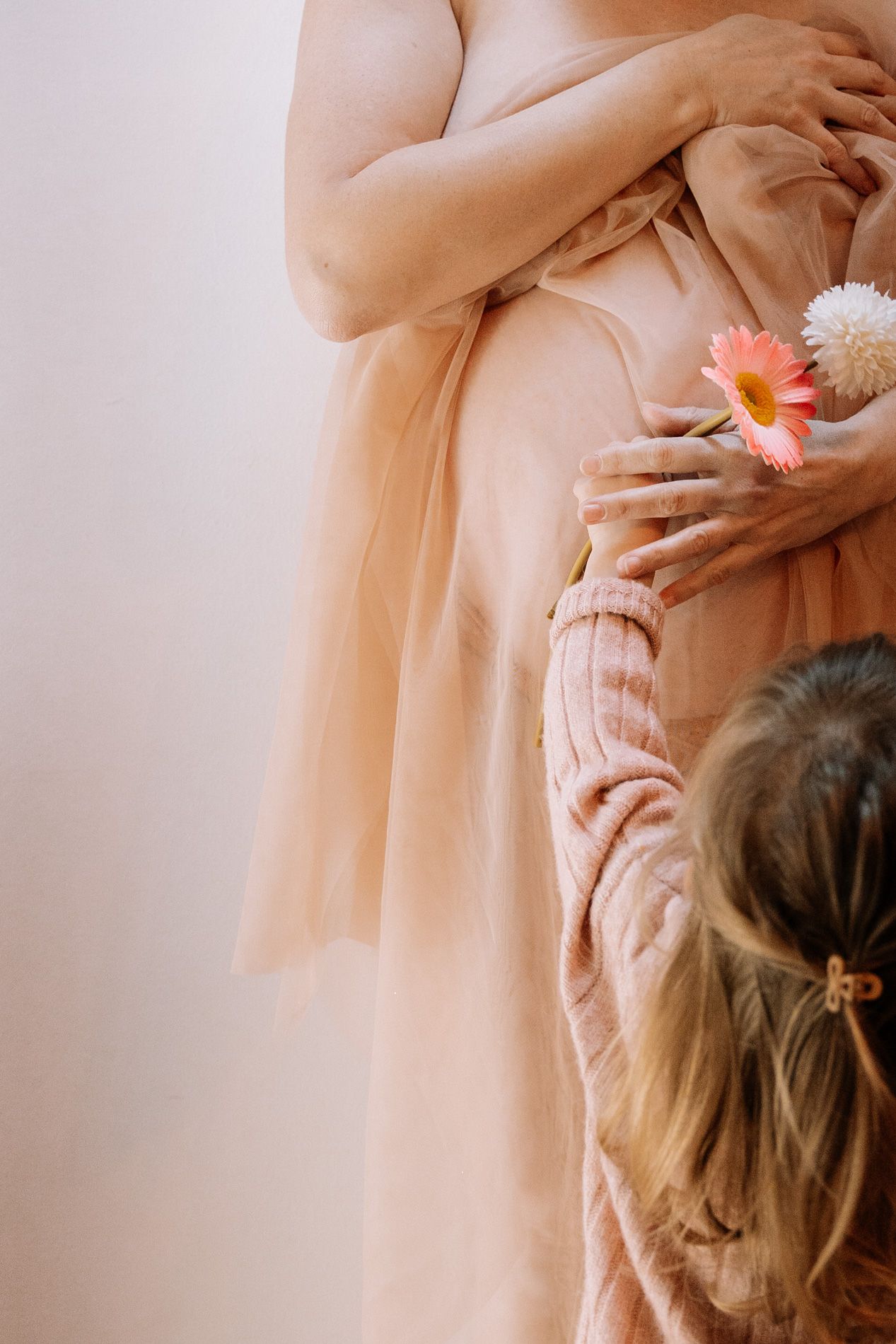 Hands gently placing delicate pink and white daisies in soft peach-toned setting.