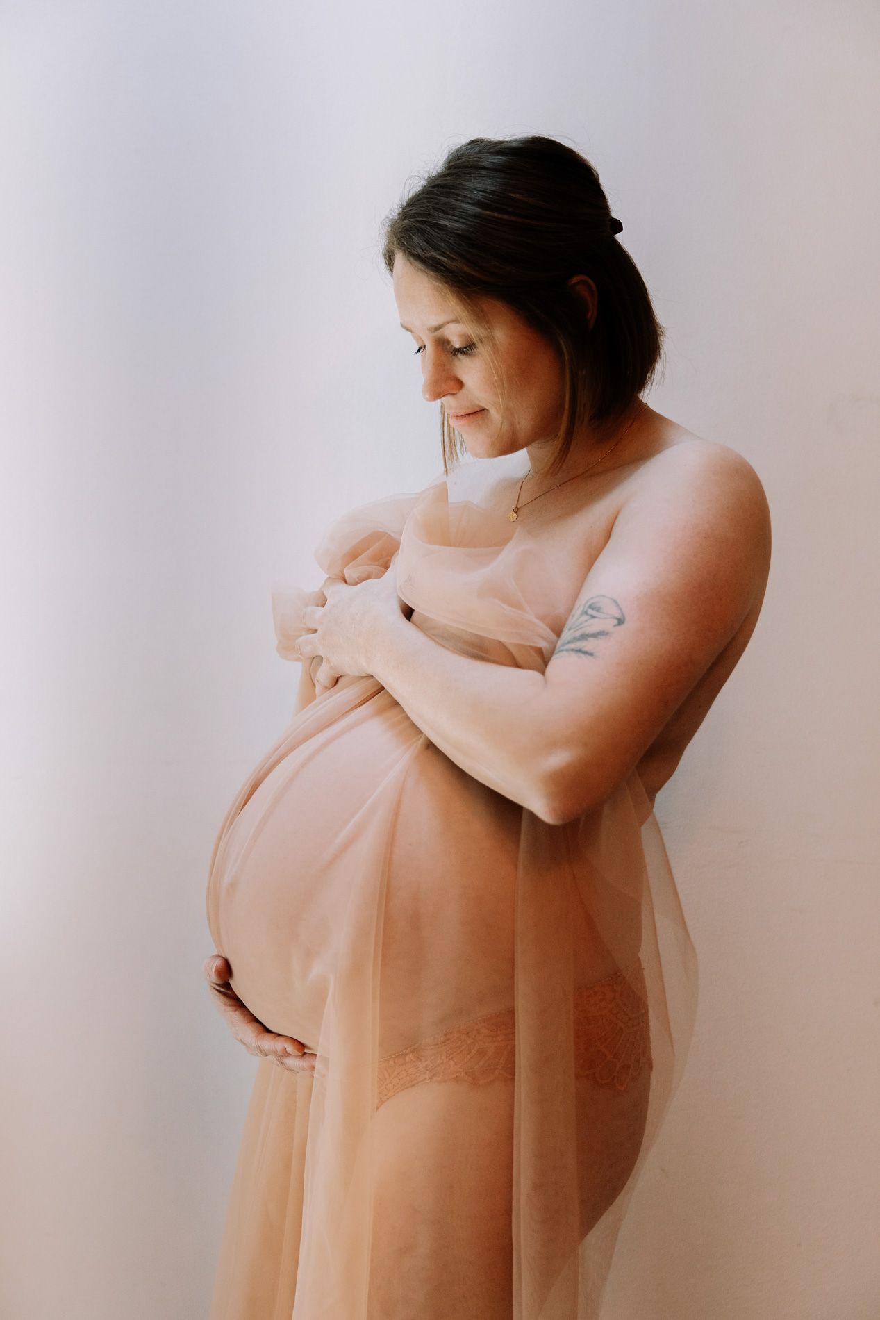 A series of maternity photos showing a pregnant woman in soft peach tulle fabric against a light background.