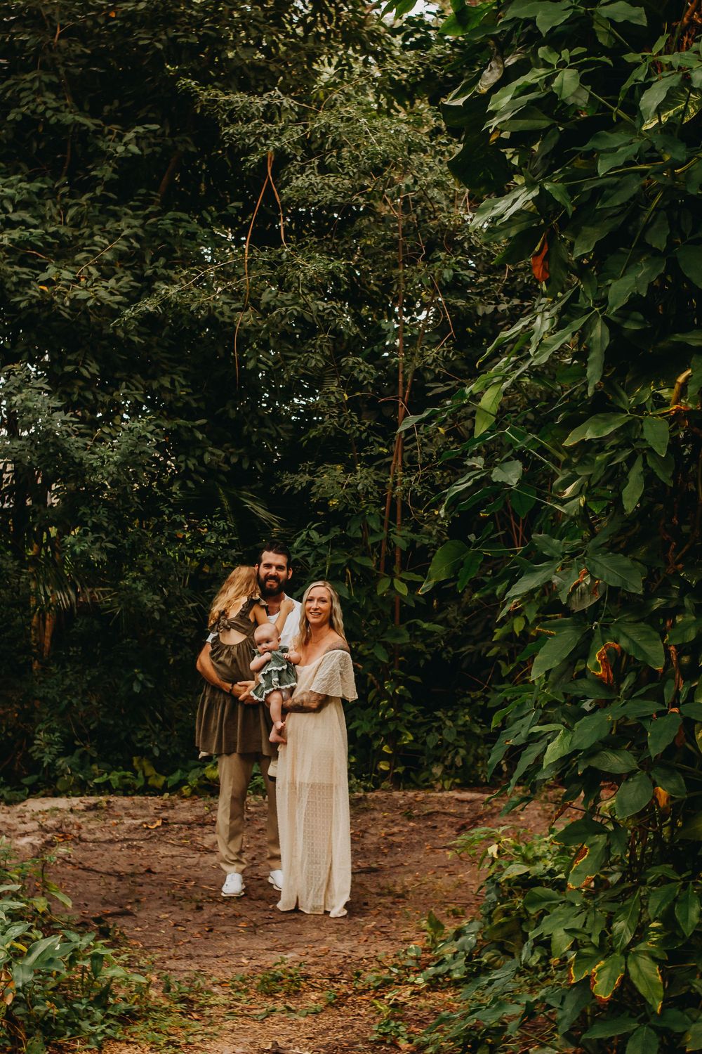A couple poses together in a lush garden setting surrounded by greenery and trees during a romantic outdoor photoshoot.