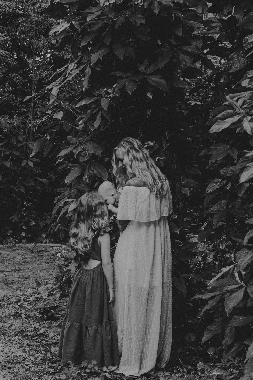A series of black and white photographs showing two figures in flowing dresses standing against a leafy backdrop.