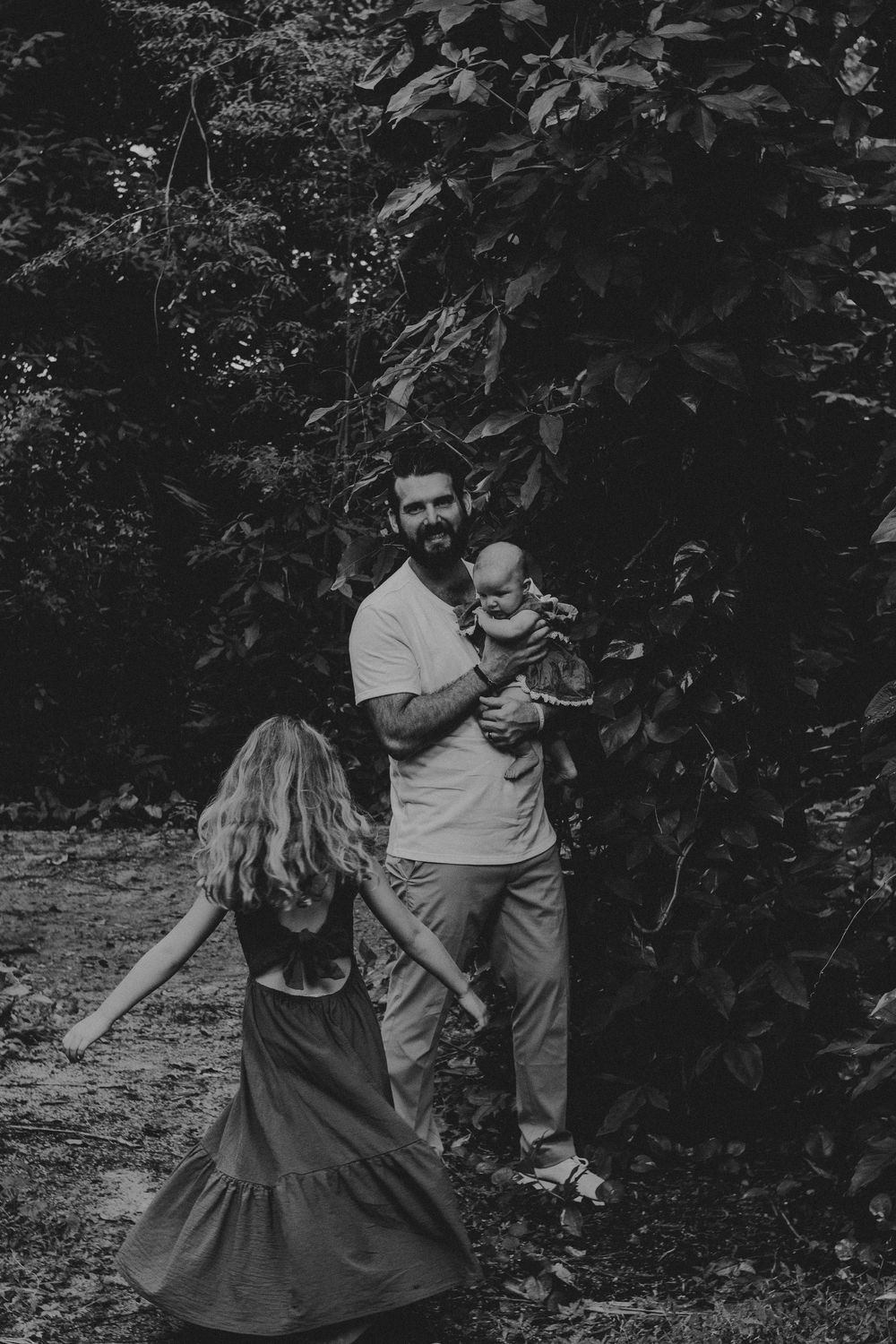A black and white photo of a family sharing playful moments in a garden setting.