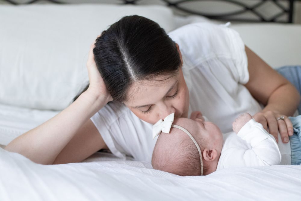 A mother laying on her side on a white bed gazing lovingly at her newborn baby.