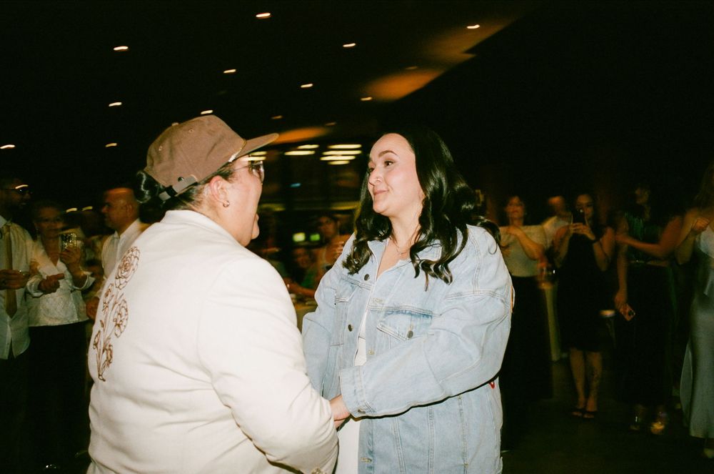 Two people in white and light blue attire dancing together in a dimly lit indoor venue.