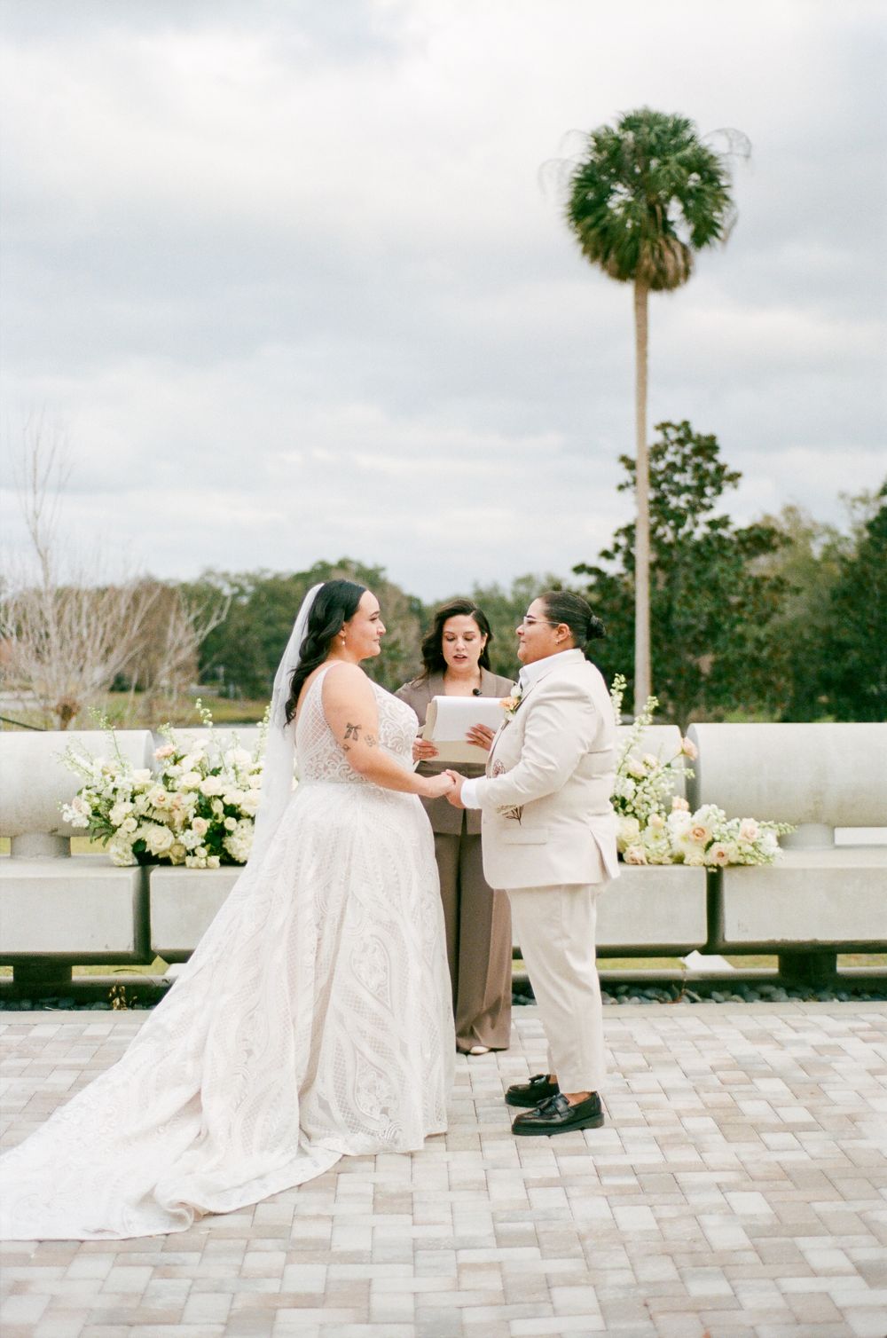 A wedding couple exchanges vows during an intimate outdoor ceremony with a palm tree backdrop.