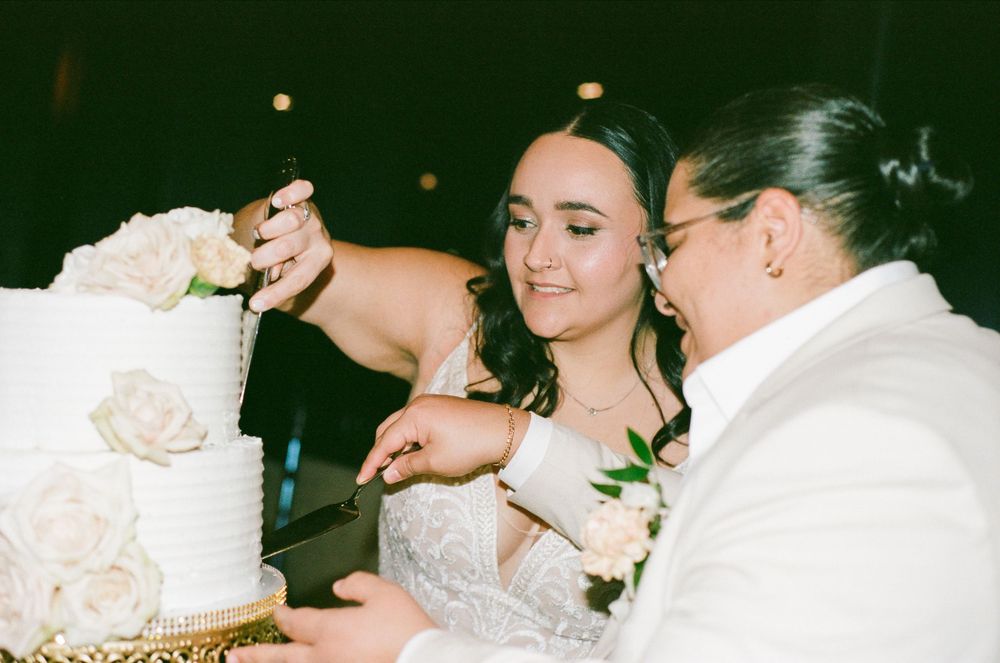 Bride and groom share a romantic moment while cutting their elegant white wedding cake together at the reception.