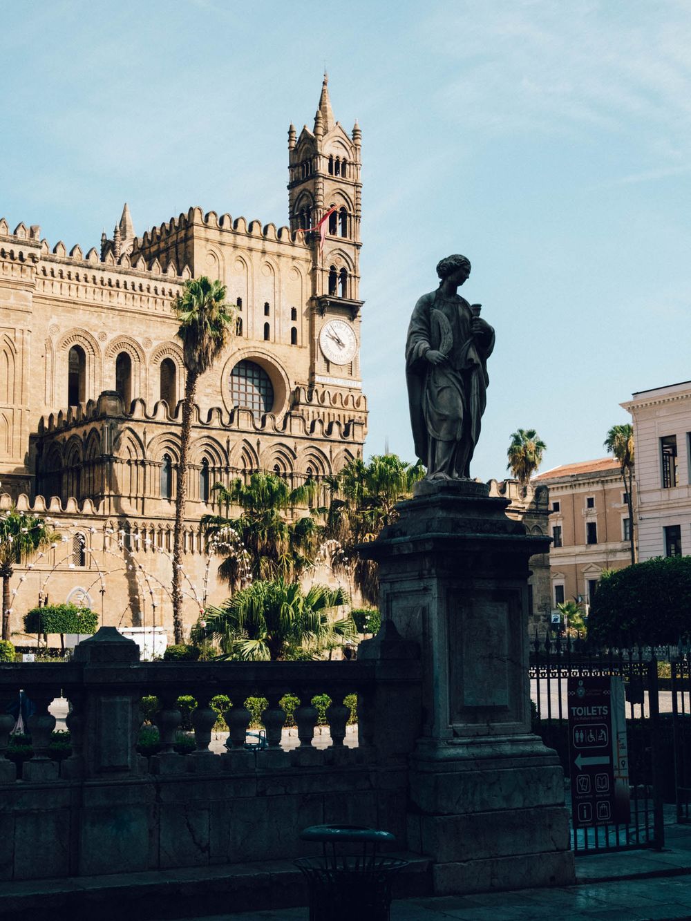 Historic Palermo Cathedral in Sicily with ornate Norman architecture and a dark statue silhouette against blue sky.