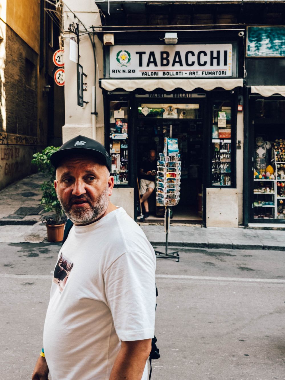 A tobacco shop (Tabacchi) storefront in Italy with a person standing outside wearing a white t-shirt and cap.
