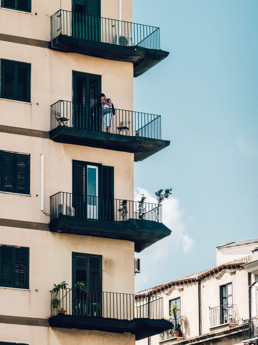 Modern apartment building with black metal balconies against bright blue sky in Mediterranean style.