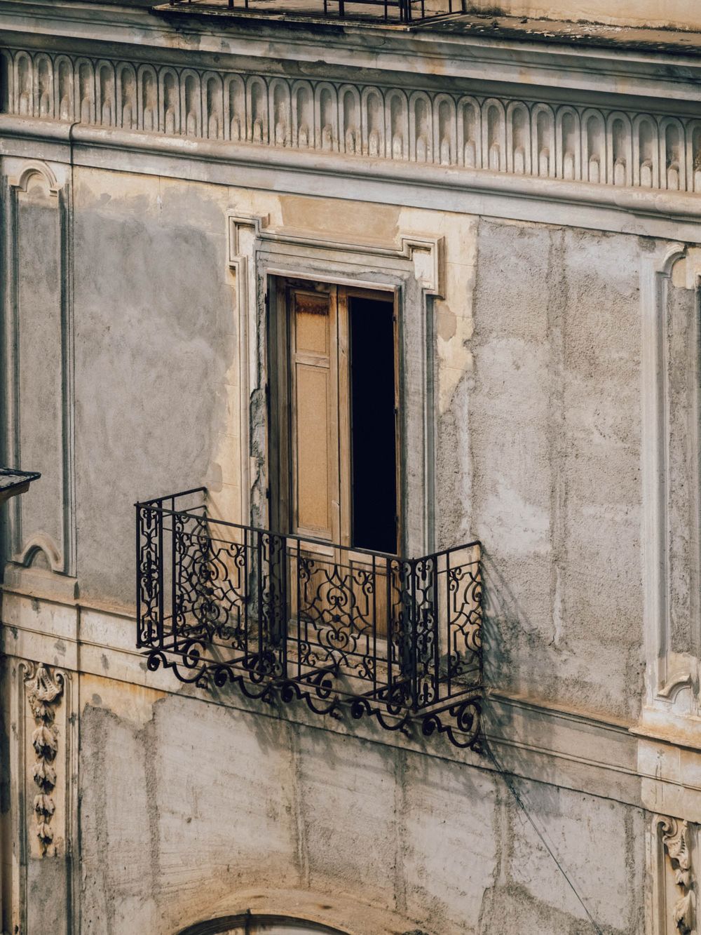 Ornate wrought iron balconies adorn a weathered beige stone building facade in European architectural style.