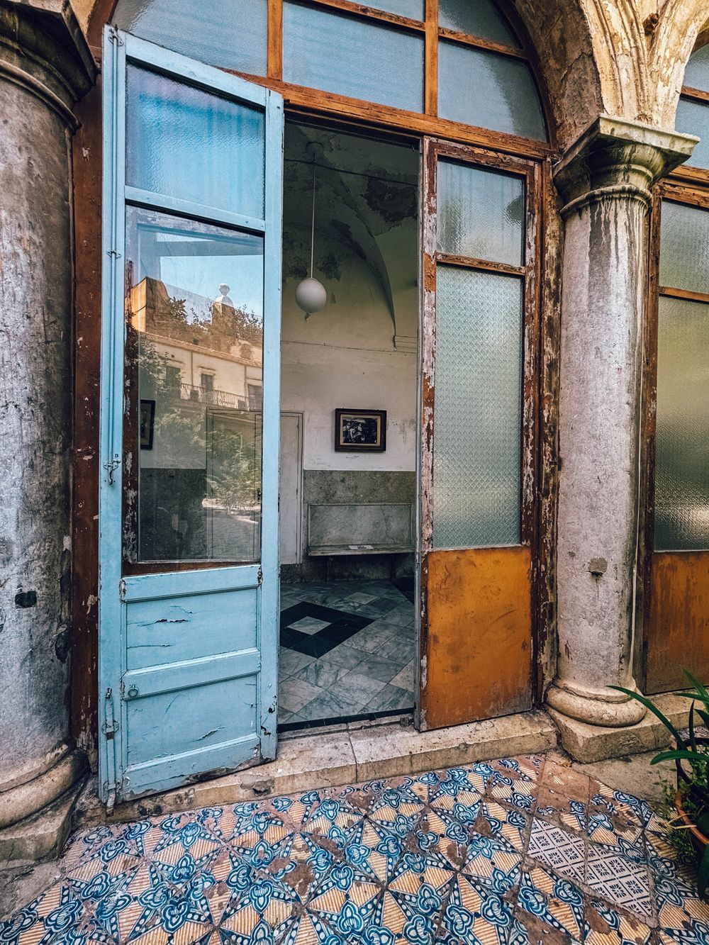 Vintage architectural details of a dilapidated hallway with ornate blue mosaic floor tiles and weathered columns.