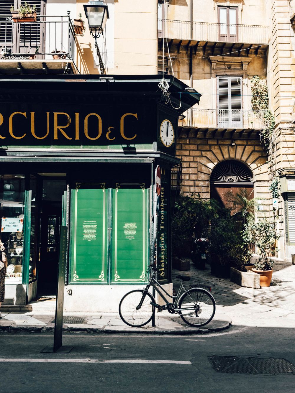 A vintage bicycle parked outside a storefront with 'Curio' signage and green shutters on a charming European street.