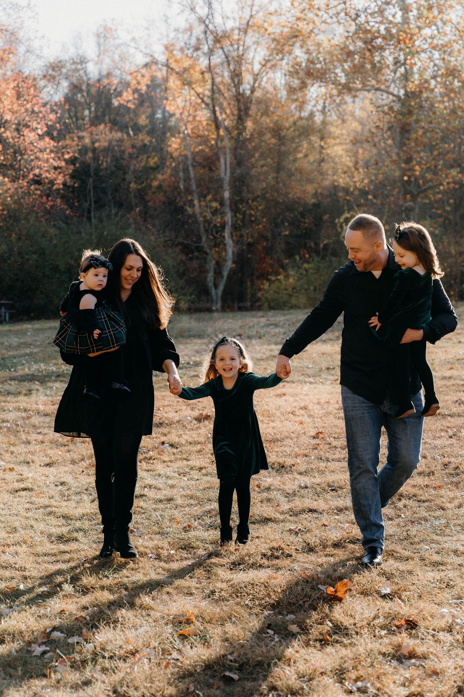 Family playing and running together on autumn grass during golden hour outdoor photoshoot.