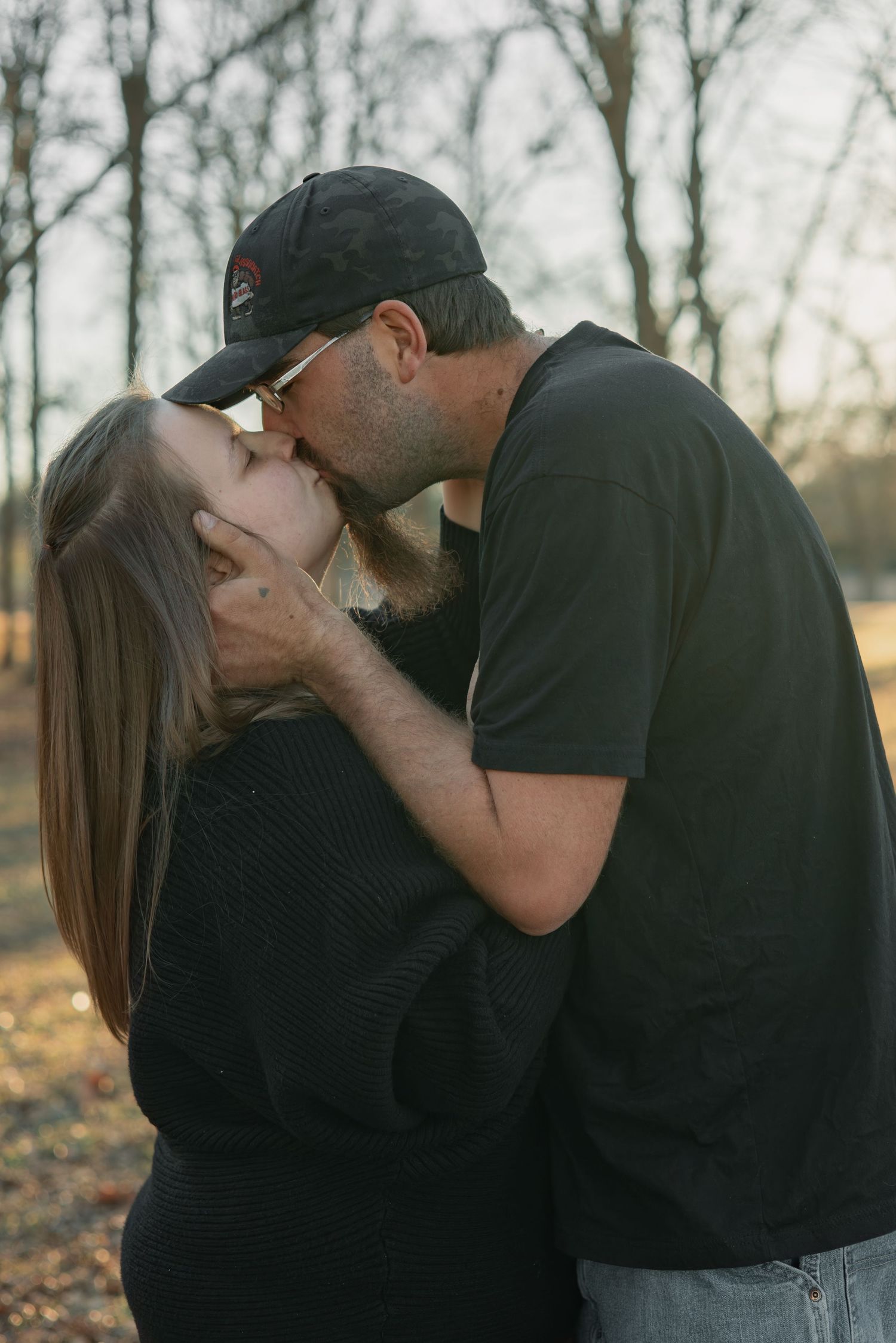 A couple in black clothing share a series of intimate kisses against a light background.
