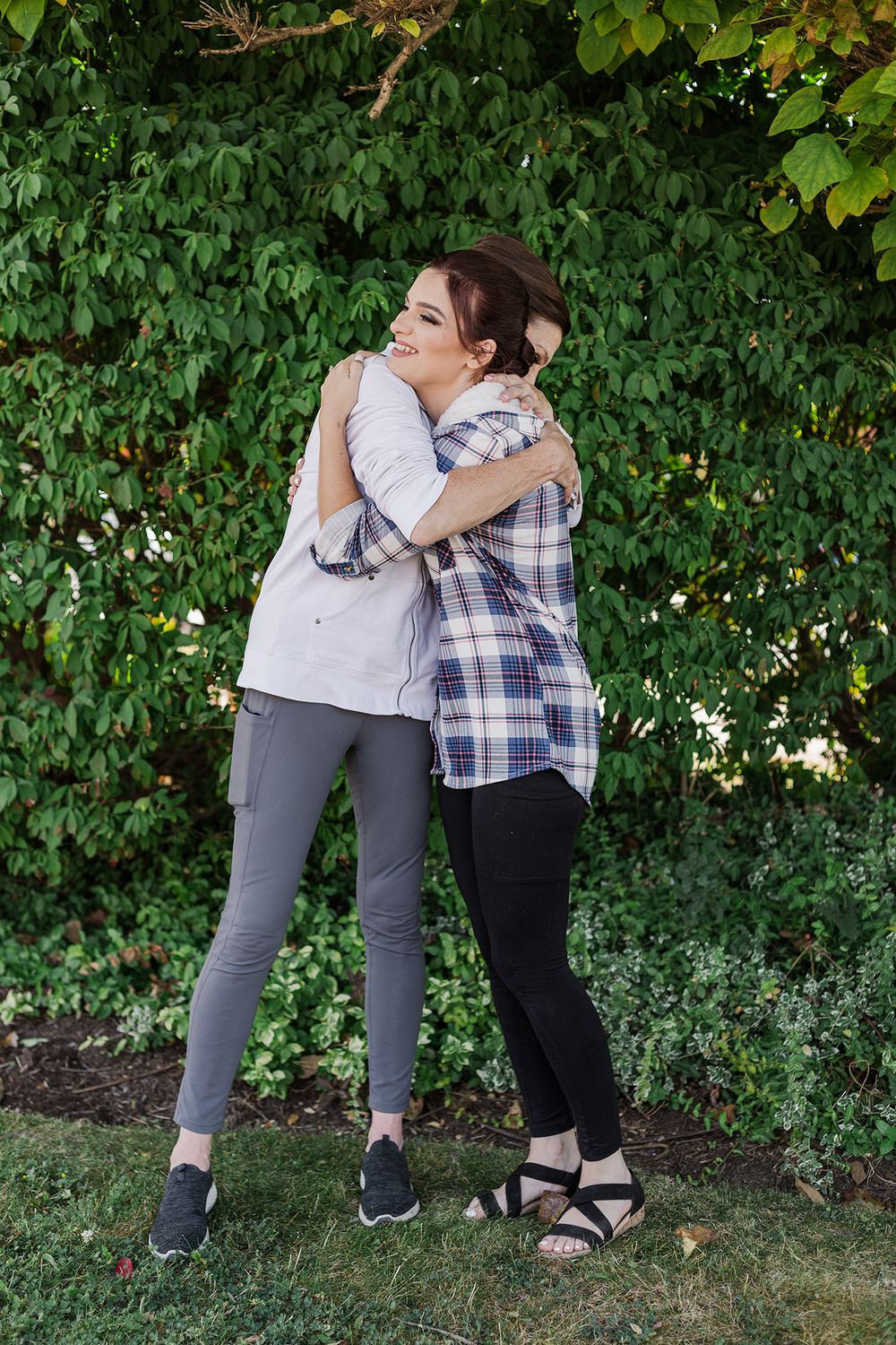 Bride hugging her mom in front of some greenery in the morning in Kitchener, Ontario.