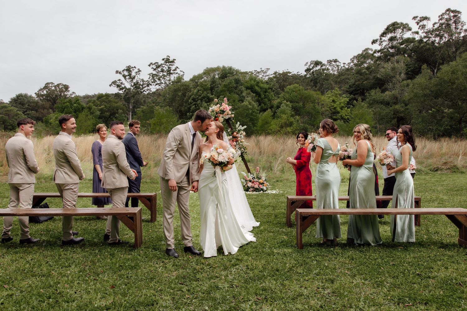 Wedding party poses together in a rustic outdoor setting with horses on a grassy hillside.