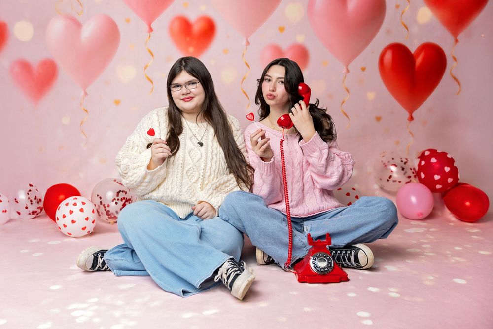 Teen girls pose with red rotary phone and heart props on pink Valentine’s Day backdrop with balloons in NH photography studio