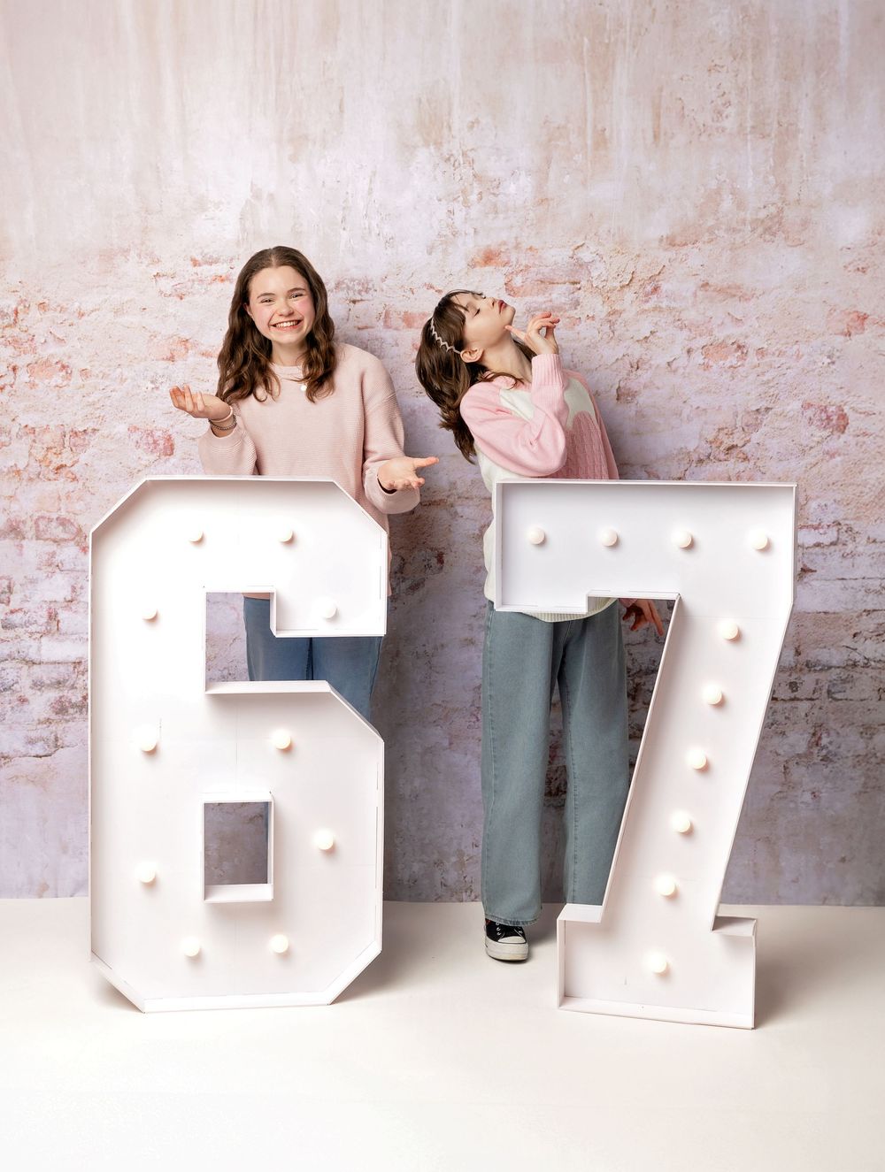 Teen best friends laugh and pose with large marquee 67 numbers on pink studio backdrop in New Hampshire