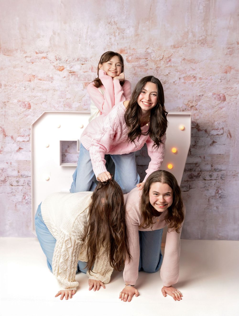 Four teen best friends pose laughing around marquee numbers on pink textured backdrop in New Hampshire photo studio