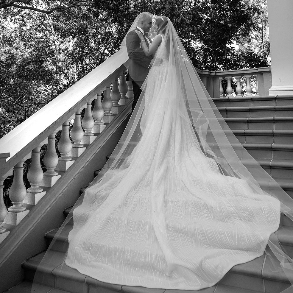 Black and white romantic wedding photo of couple kissing on stone staircase with long flowing veil.