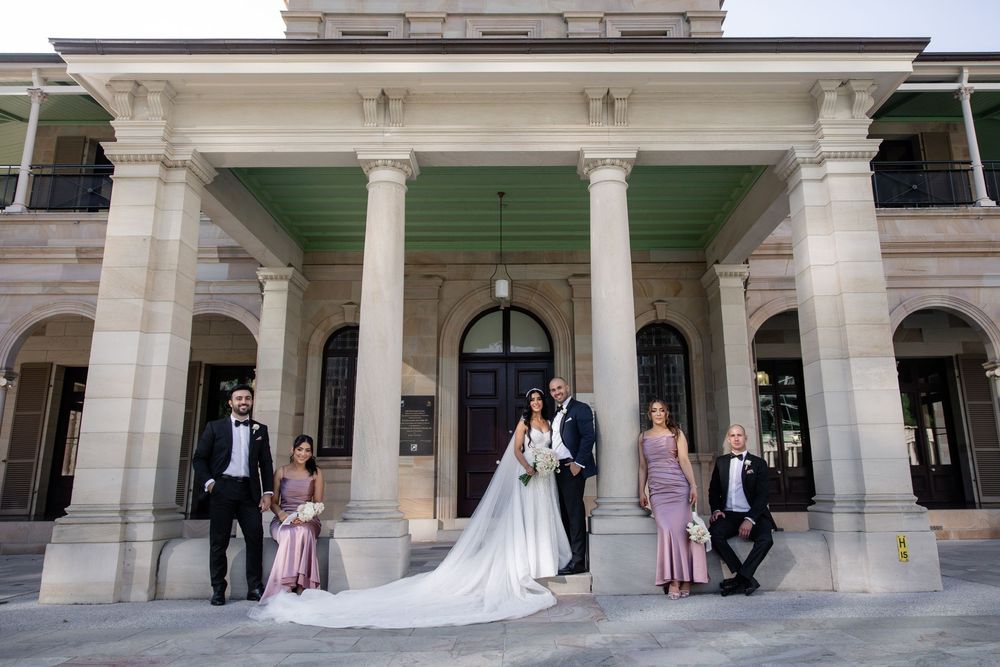 Wedding party poses in front of a grand colonial building with tall white columns on their special day.