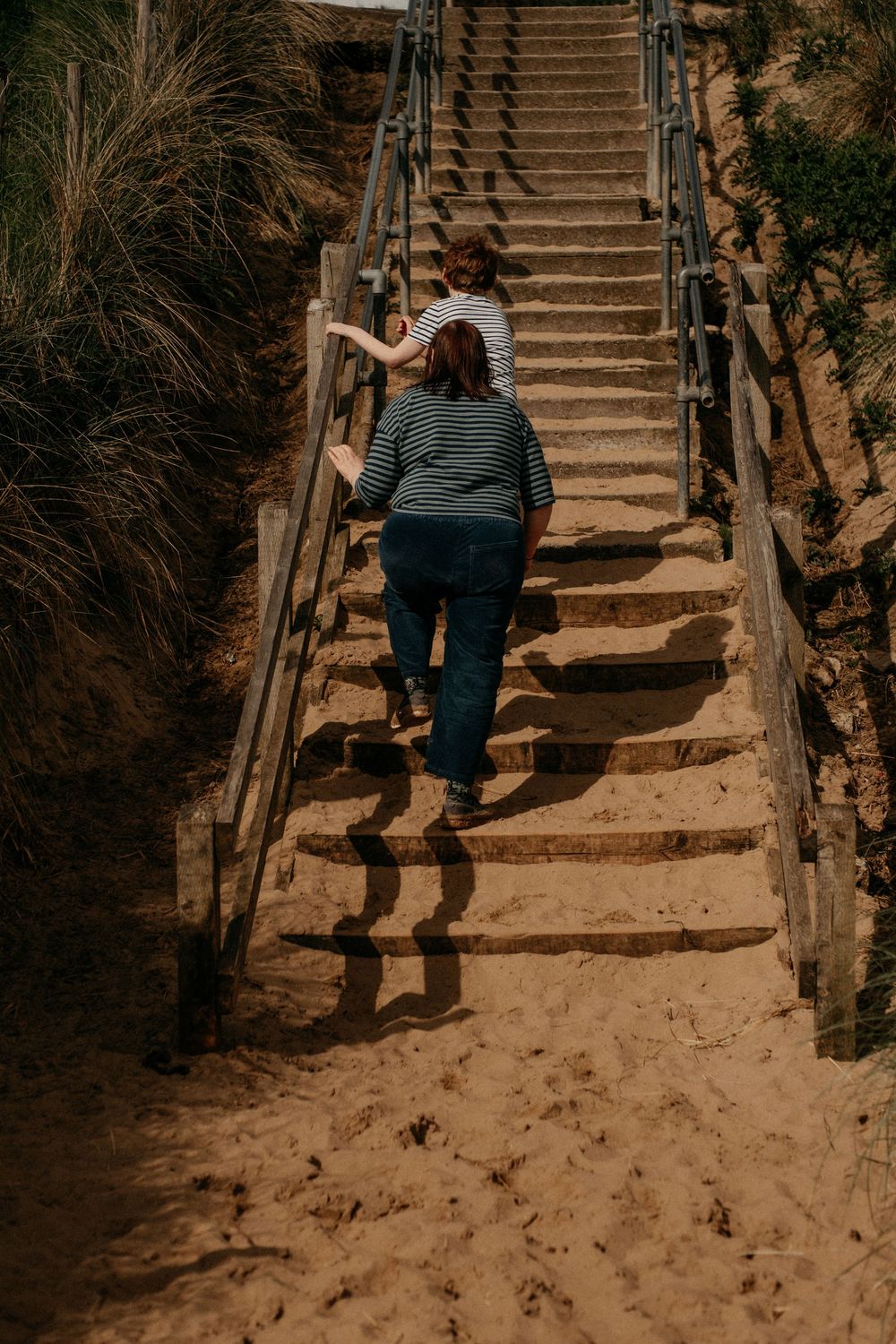 Mother and autistic son walking up wooden walkway from the beach - tynemouth