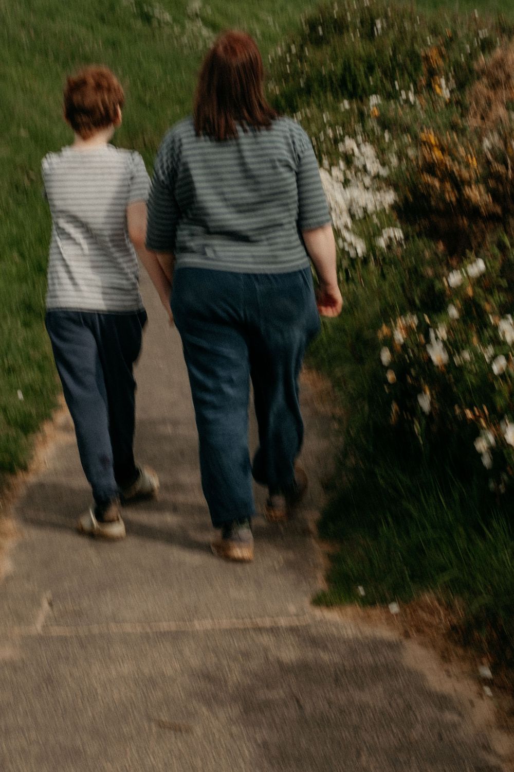 Mother and autistic son walking down a path with flowers
