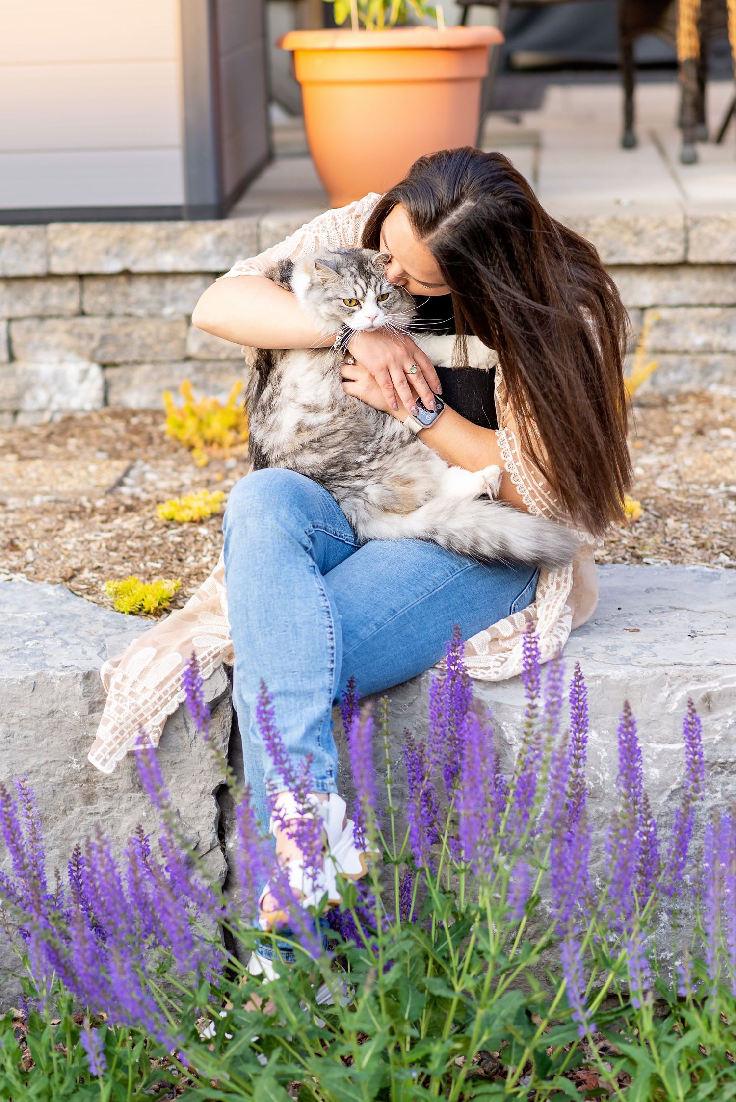A cat and owner share a tender moment among purple flowers on stone steps.