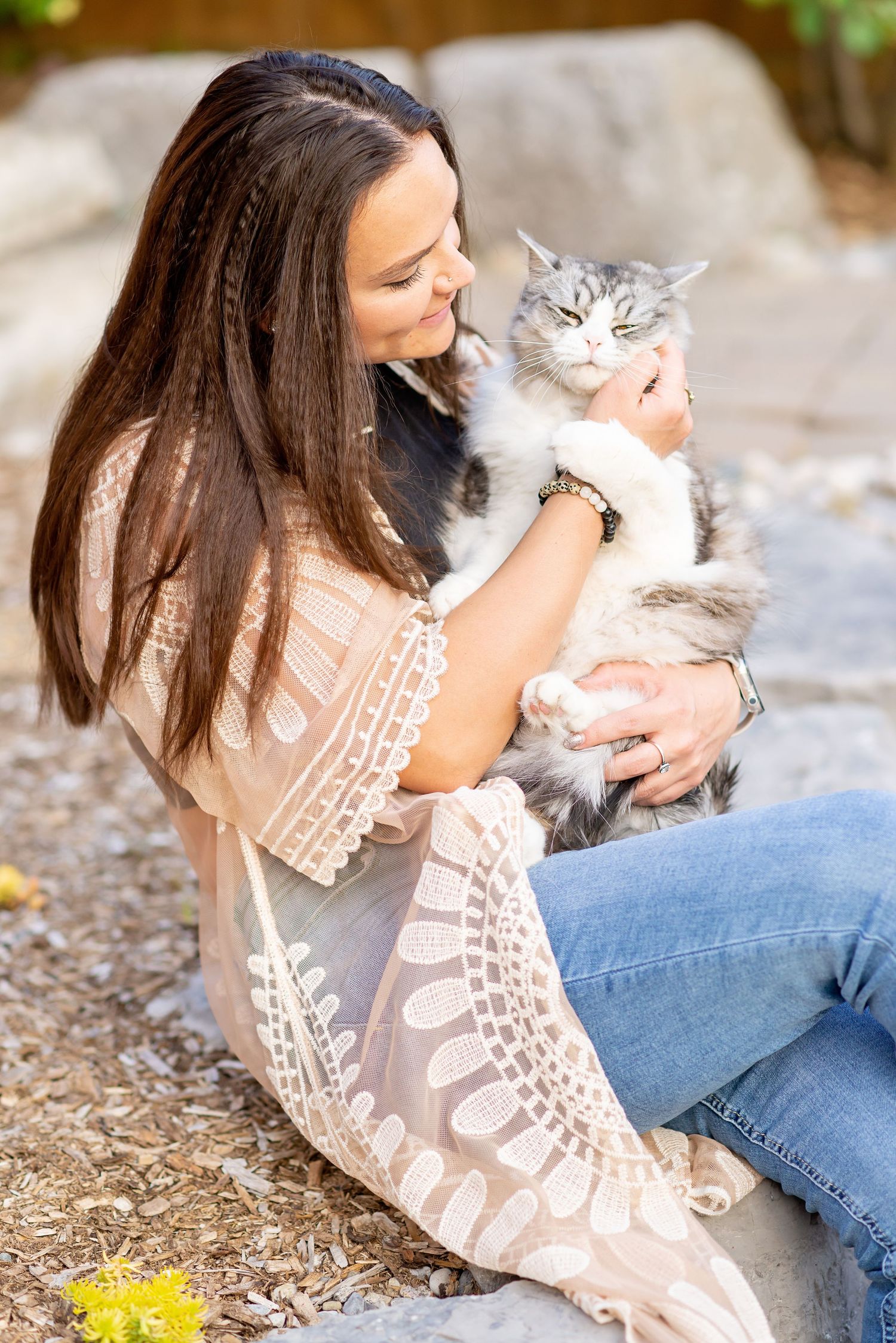 A fluffy white and gray cat being held and petted while sitting outdoors on a sunny day.