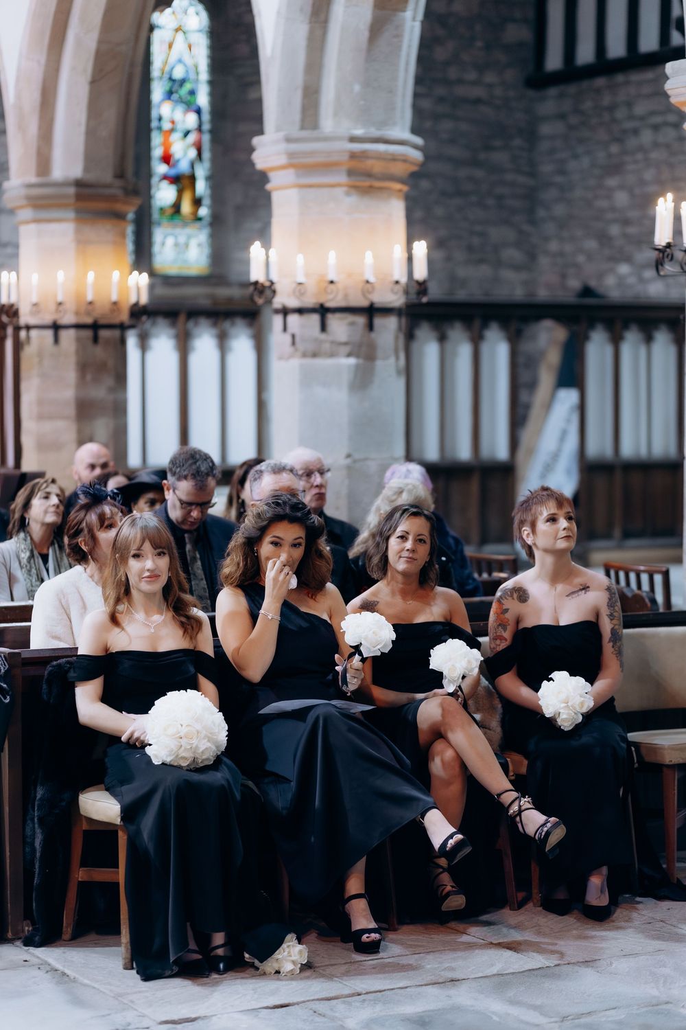 Wedding guests in black dresses seated in church pews during an elegant ceremony.