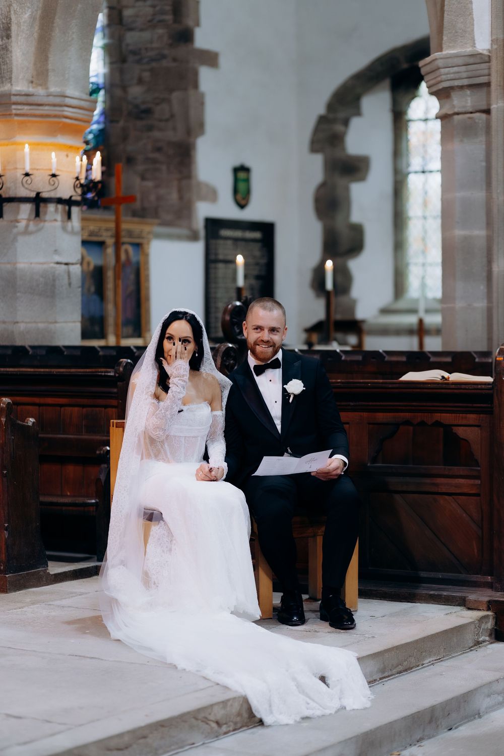 Couple seated on church steps during their wedding ceremony surrounded by classic stone architecture.