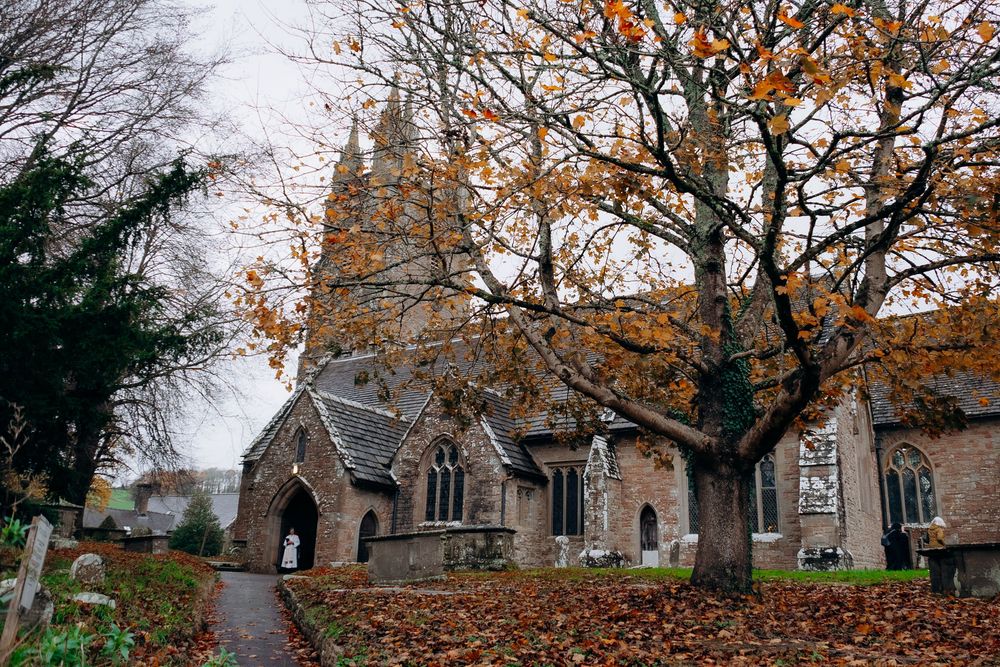 Autumn trees and fallen leaves surround a historic stone church exterior.