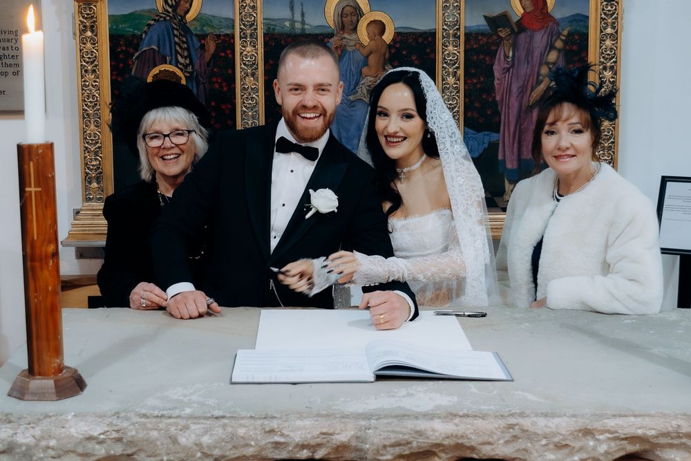 Wedding party poses for formal portraits against a white wall with religious artwork.