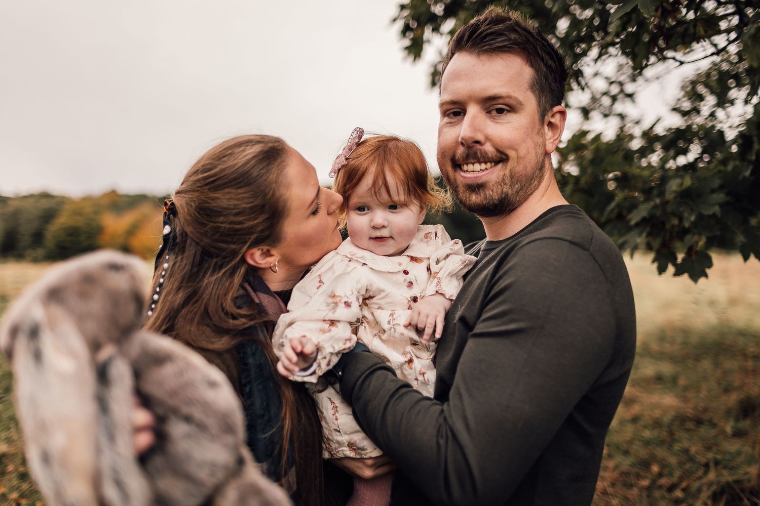 Family walks together through an autumn field with golden foliage in the background.