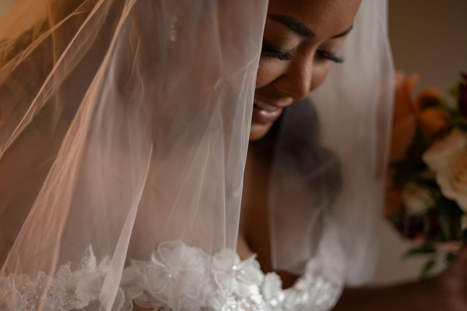 A joyful bride smiles beneath her delicate white veil during an intimate wedding moment.