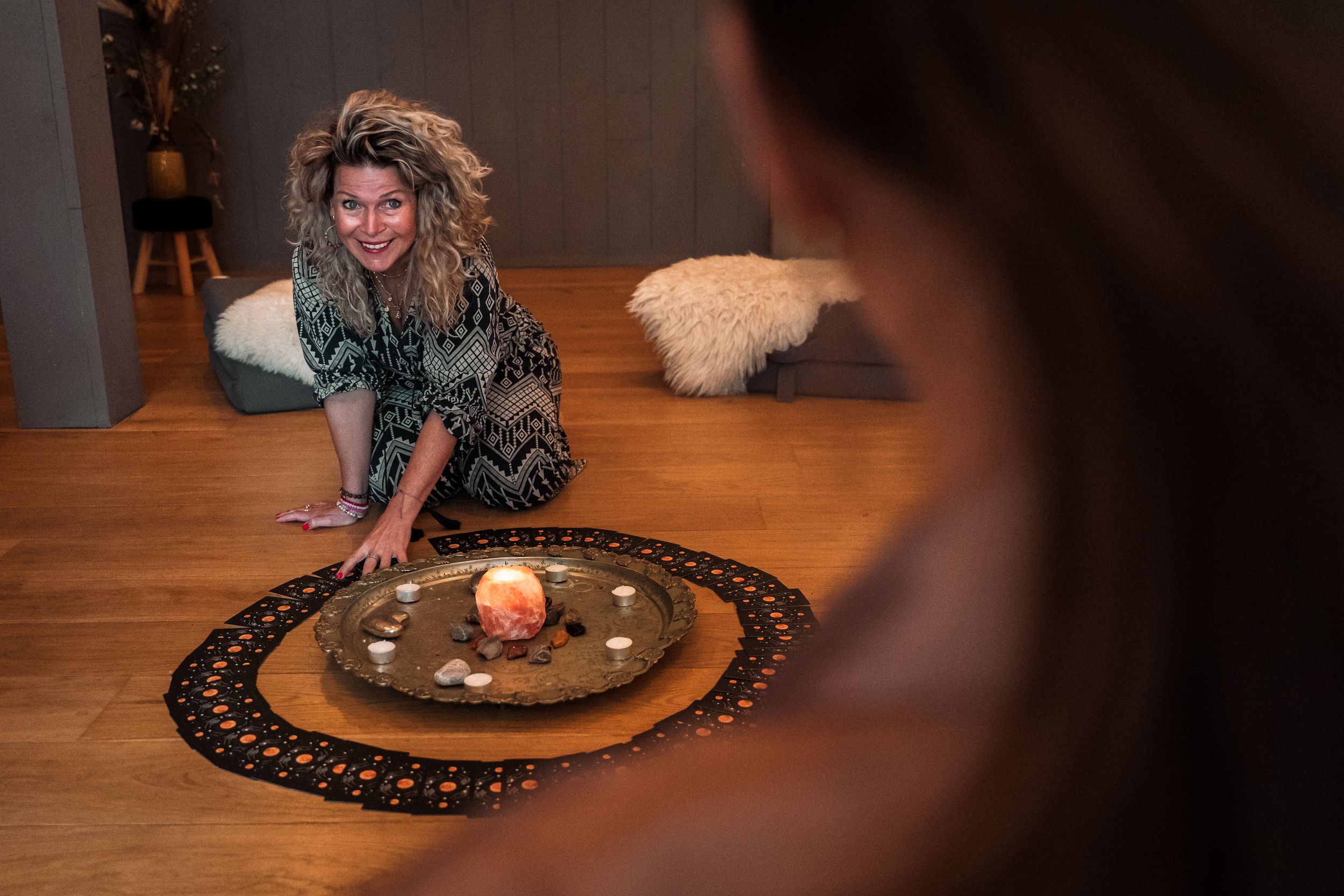 Someone reaches toward a decorative plate with candles and crystals arranged on a hardwood floor during a ritual setup.