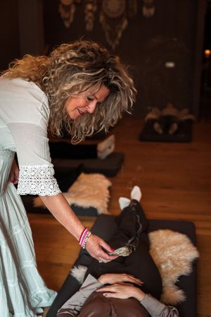 A person in a white lace top pets a small black cat on a wooden floor.