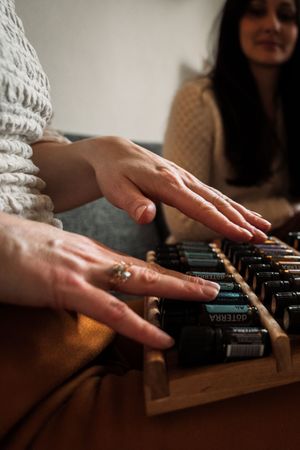 Hands with delicate rings play an old wooden typewriter keyboard in warm lighting while someone watches.