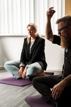 Two people sitting on purple yoga mats during a meditation or wellness session in a bright room.