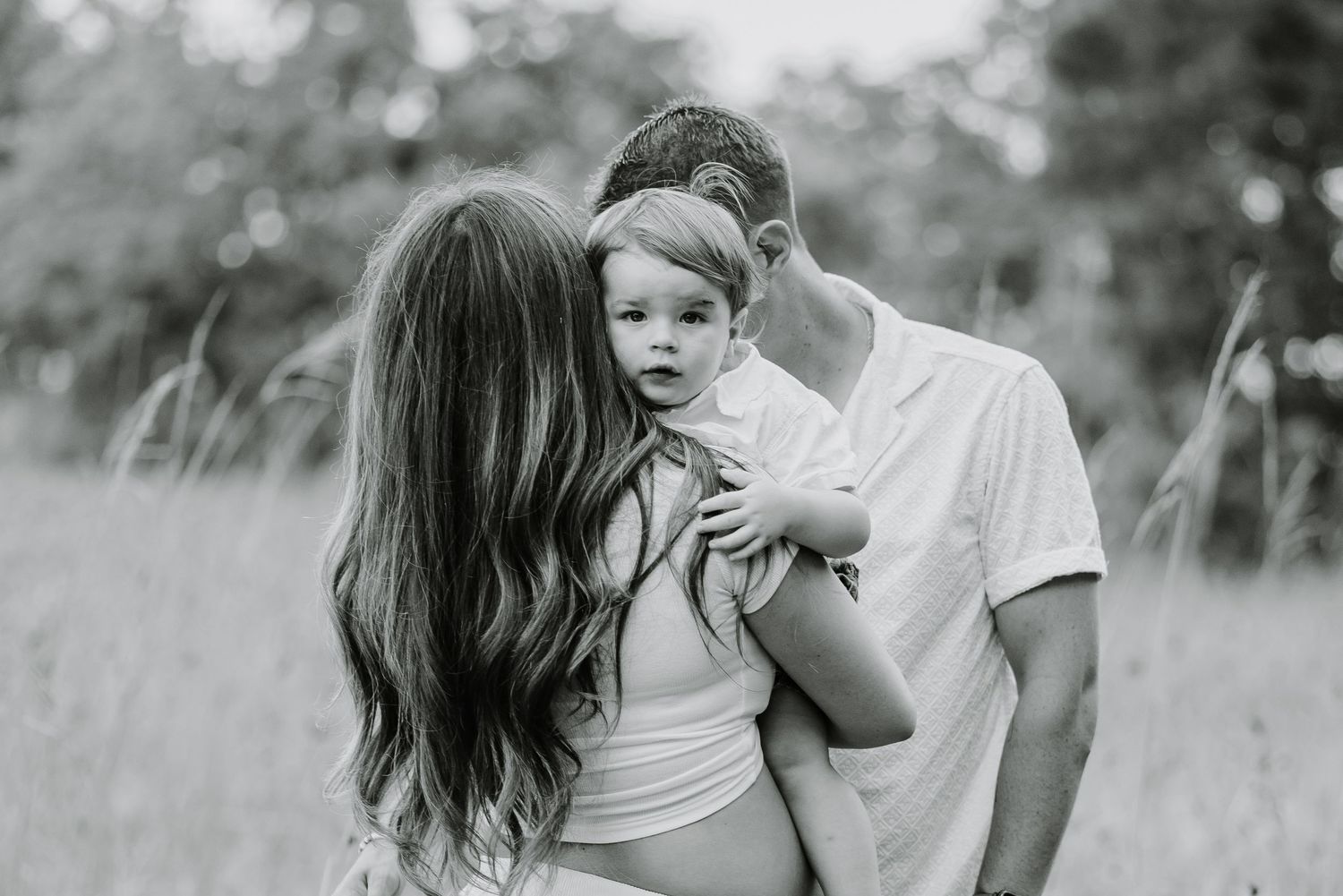 Black and white photo collage showing tender family moments in a grassy field during golden hour.