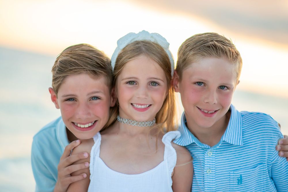 Four smiling children pose together outdoors against a soft sunset sky in matching blue and white outfits.