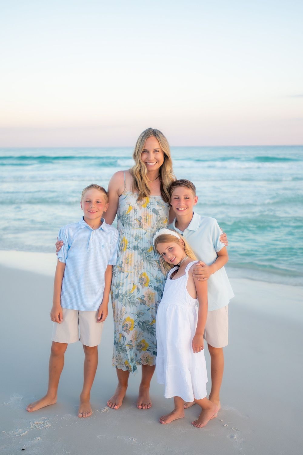 A family poses together on a beautiful beach at sunset with turquoise waters and soft sand in the background.