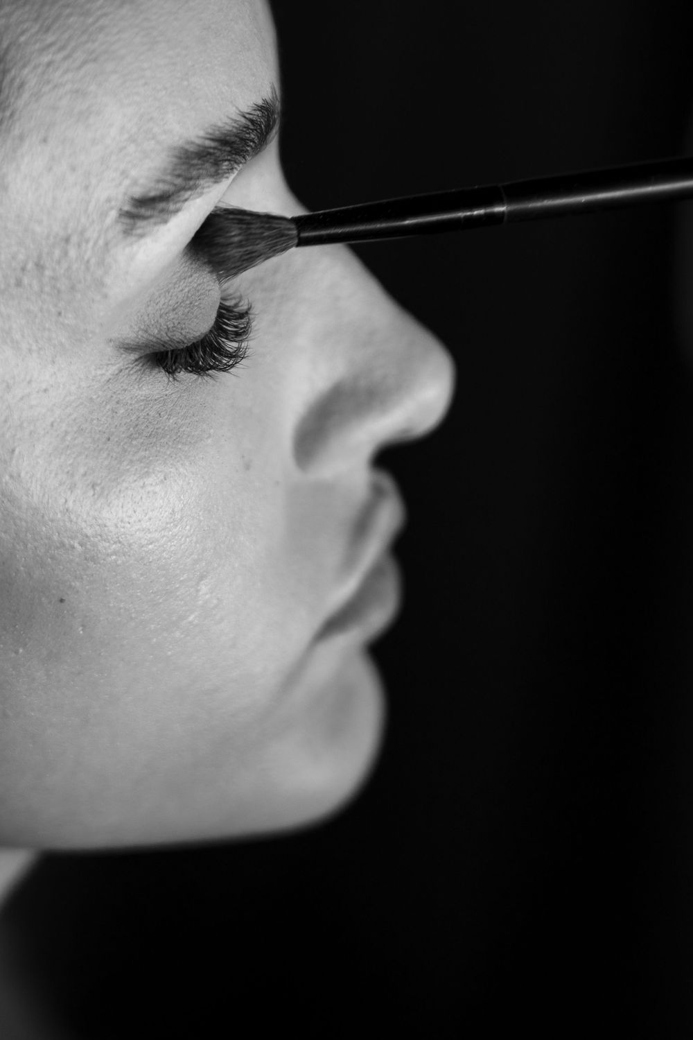 Black and white close-up profile view showing application of mascara to eyelashes.