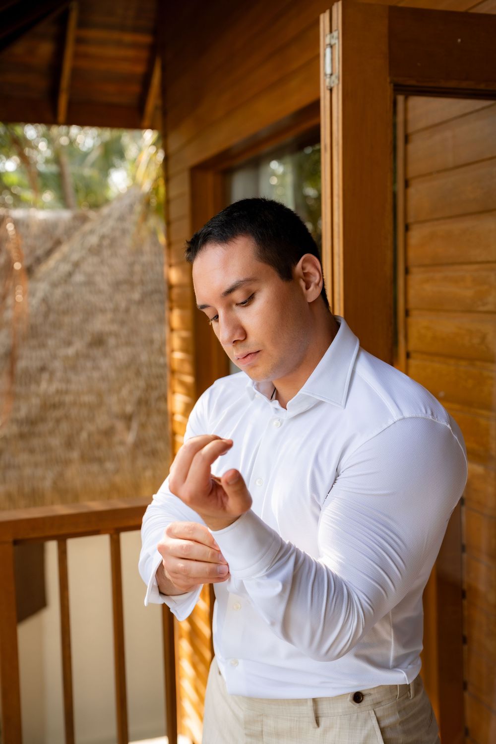 A person in a crisp white dress shirt adjusts their cuff while standing in a wooden-framed doorway.