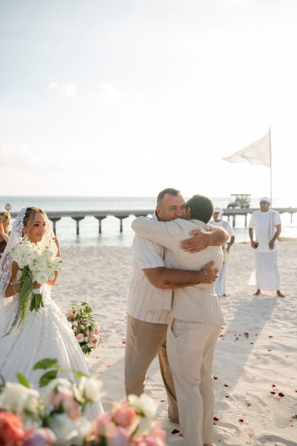 A romantic beach wedding ceremony with guests in white attire throwing rose petals as the couple embraces on the sand.