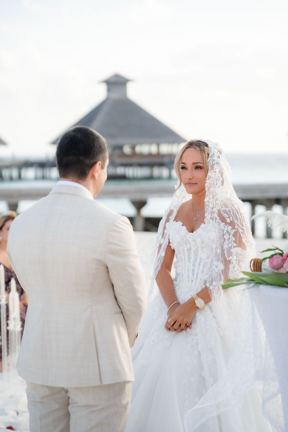 Newlyweds share intimate moments on a beach during sunset with palm trees and ocean views in the background.